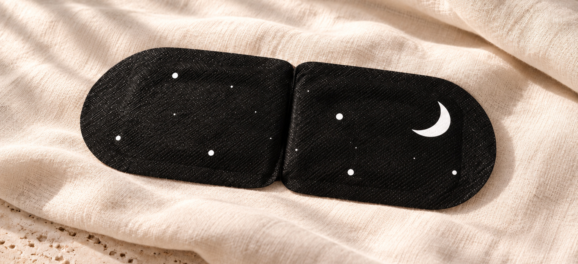 Folded EVOURA steam eye mask with its moon and star pattern resting on soft fabric